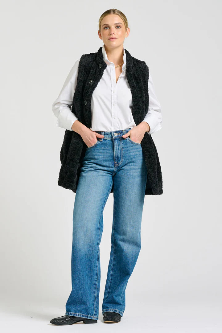 Woman wearing a black coat, white shirt, and blue jeans on a white background