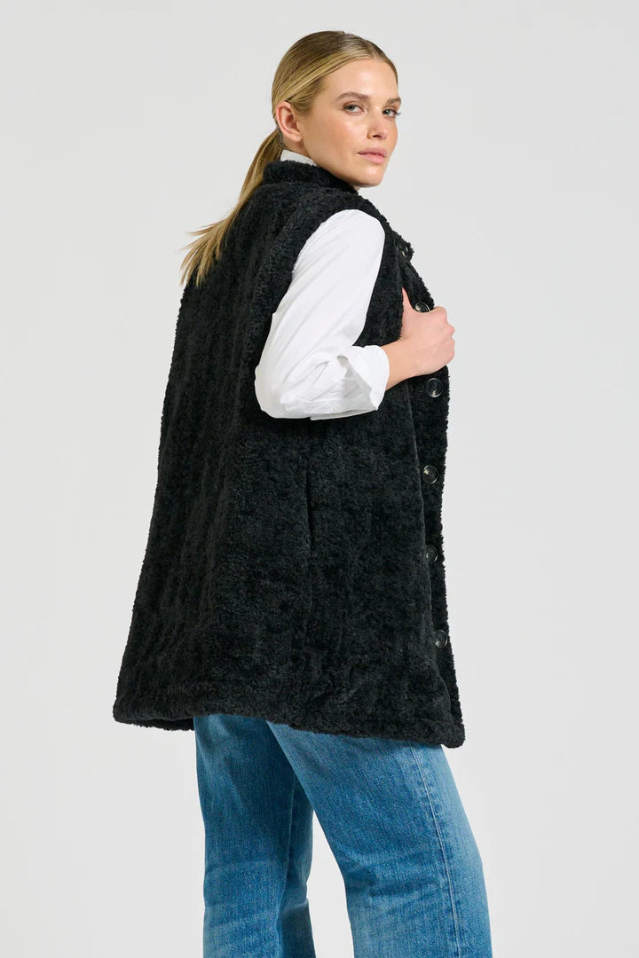Woman wearing a black fleece vest over a white shirt and blue jeans on a light gray background