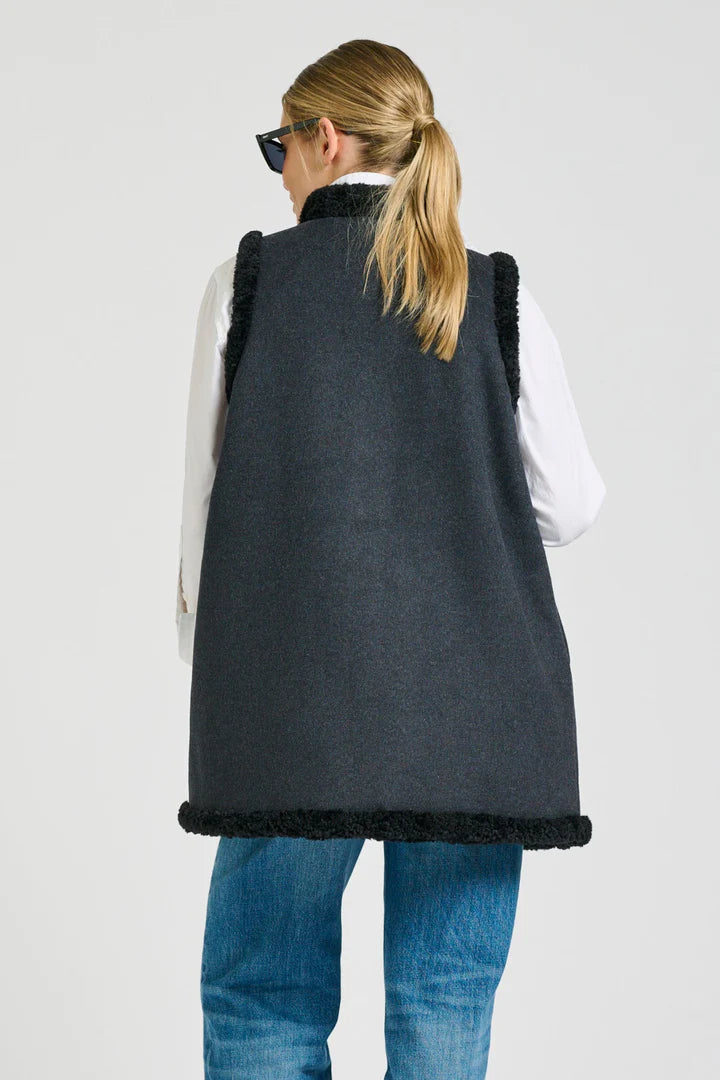 Person wearing a dark gray vest with black trim on a plain background