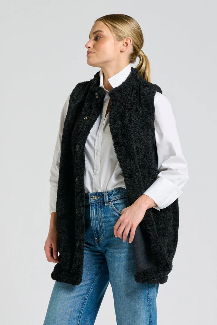 Woman wearing a black vest over a white shirt and blue jeans on a light gray background