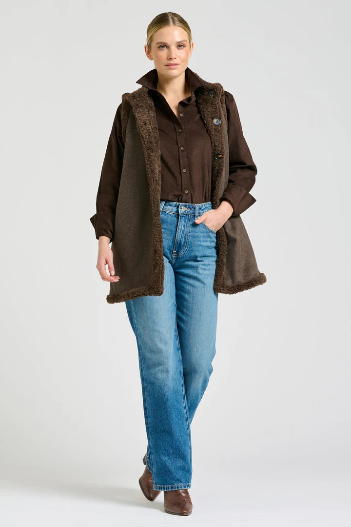 Woman wearing a brown coat with fur trim, brown shirt, and blue jeans on a white background