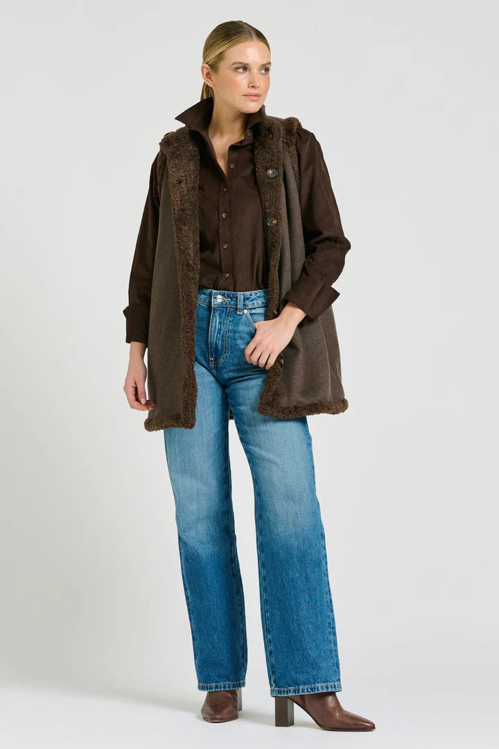 Woman wearing a brown jacket over a brown shirt with blue jeans on a white background