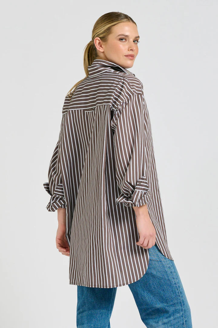 Woman wearing a long, striped shirt with rolled-up sleeves on a plain background