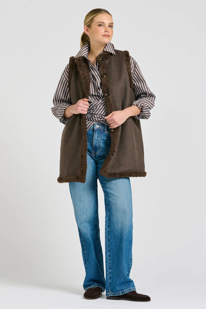Woman wearing a brown vest over a striped shirt with blue jeans on a white background