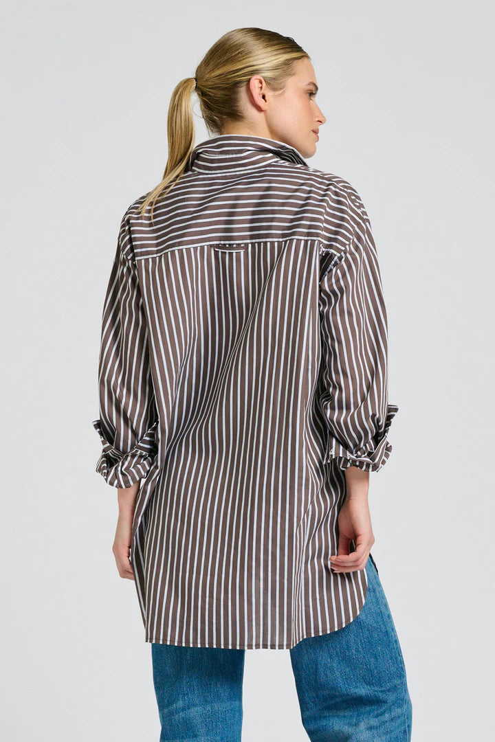 Woman wearing a long, striped shirt with rolled-up sleeves on a plain background