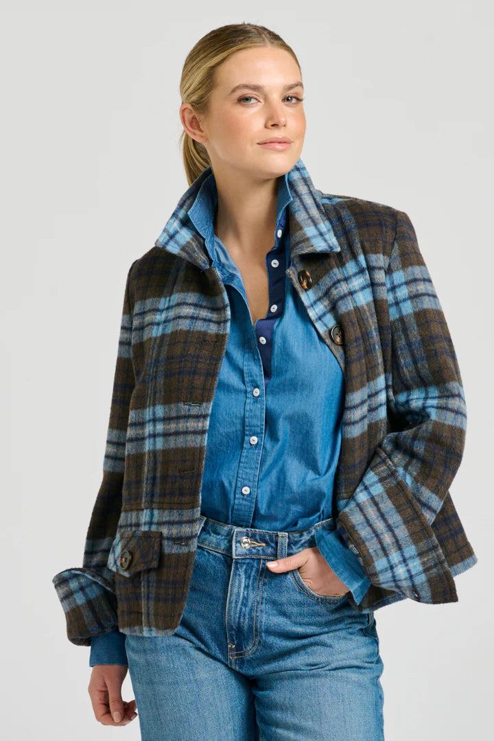 Woman wearing a plaid jacket over a blue shirt and jeans on a gray background