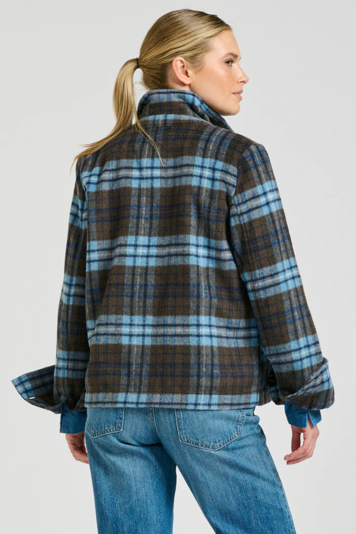 Person wearing a plaid jacket and blue jeans on a plain background