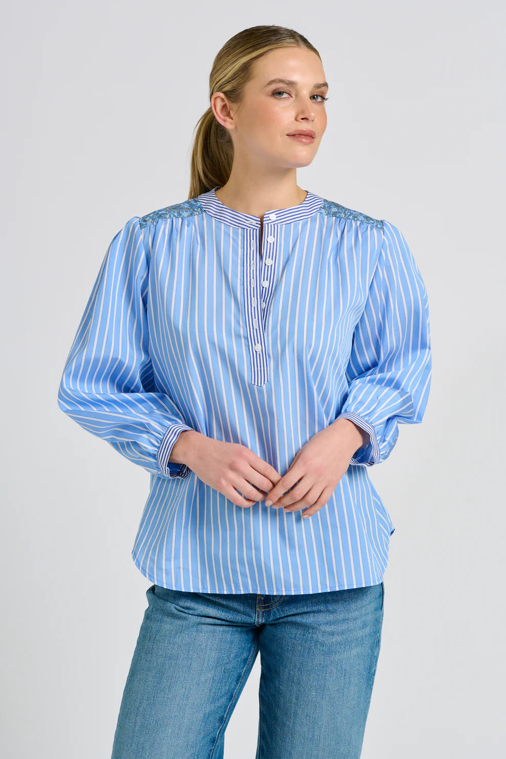 Woman wearing a blue and white striped blouse with rolled-up sleeves on a plain background