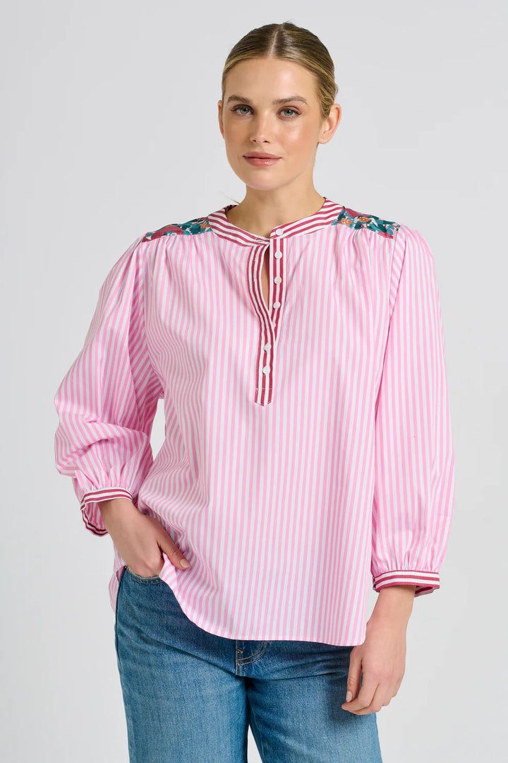 Woman wearing a pink and white striped blouse with decorative trim on a gray background