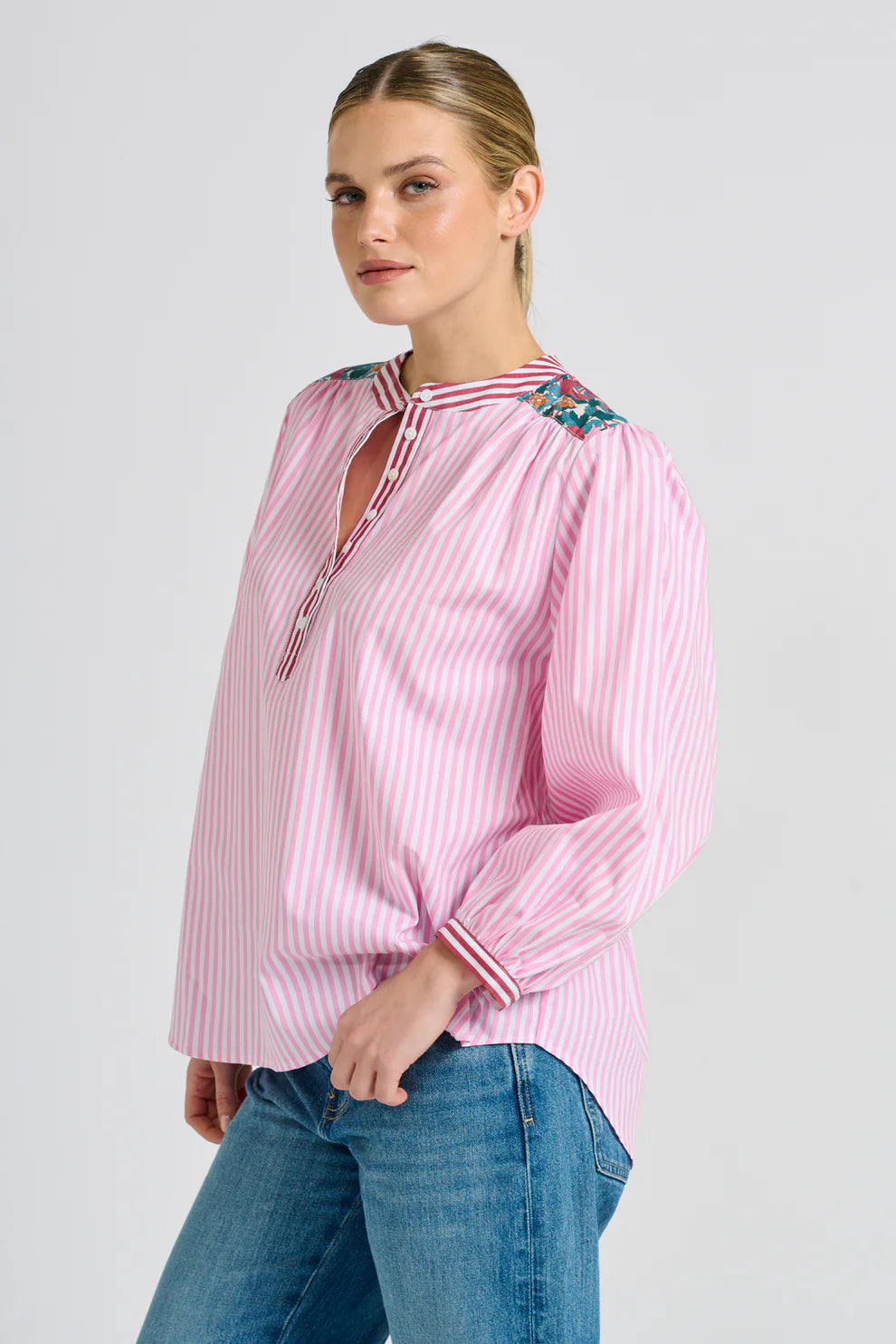 Woman wearing a pink striped blouse with floral accents on a white background