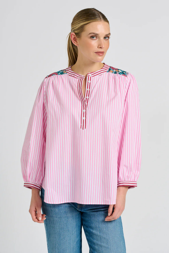 Woman wearing a pink and white striped blouse with floral accents on a gray background