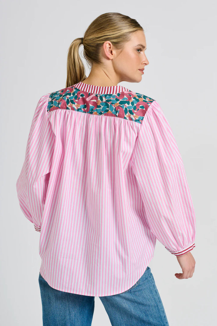 Woman wearing a pink striped blouse with floral embroidery on a plain background