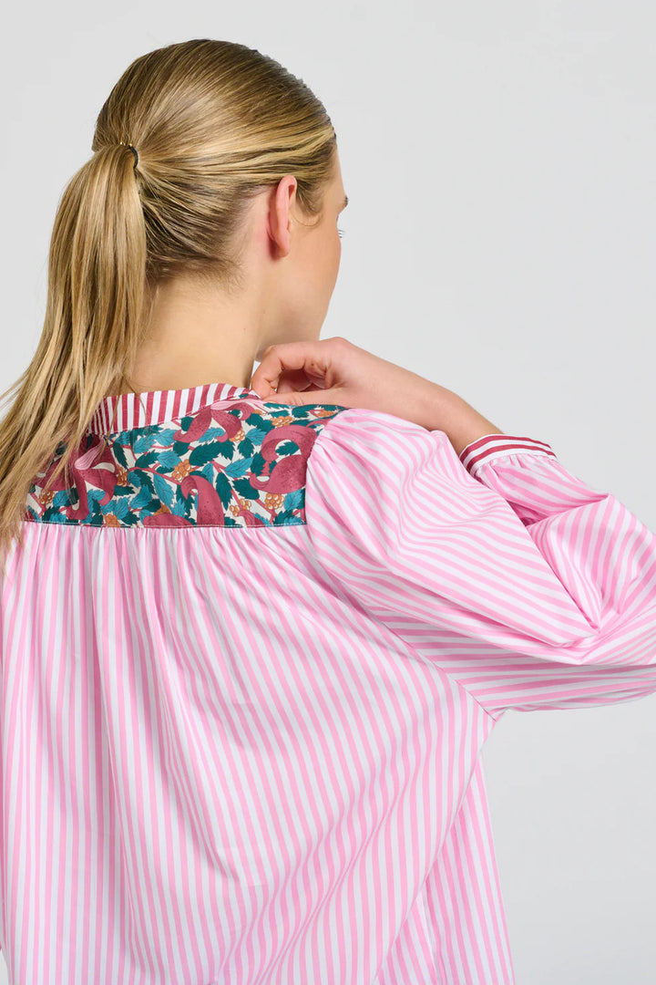 Woman wearing a pink and white striped shirt with floral trim on a light gray background