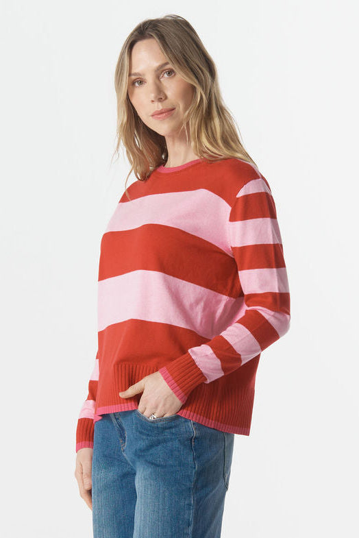 Woman wearing a red and pink striped sweater and blue jeans on a white background