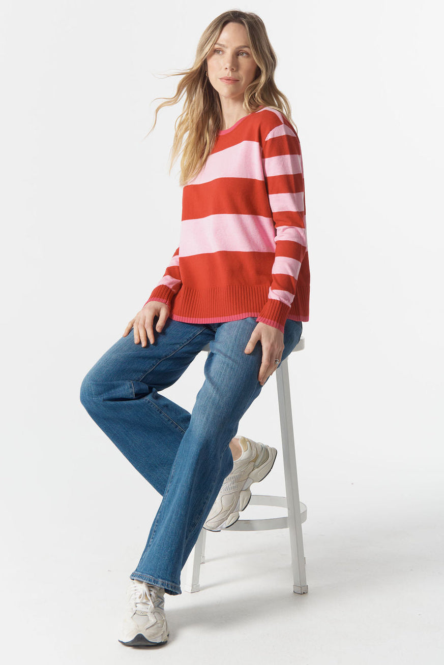 Woman wearing a red and white striped sweater and blue jeans sitting on a stool against a white background