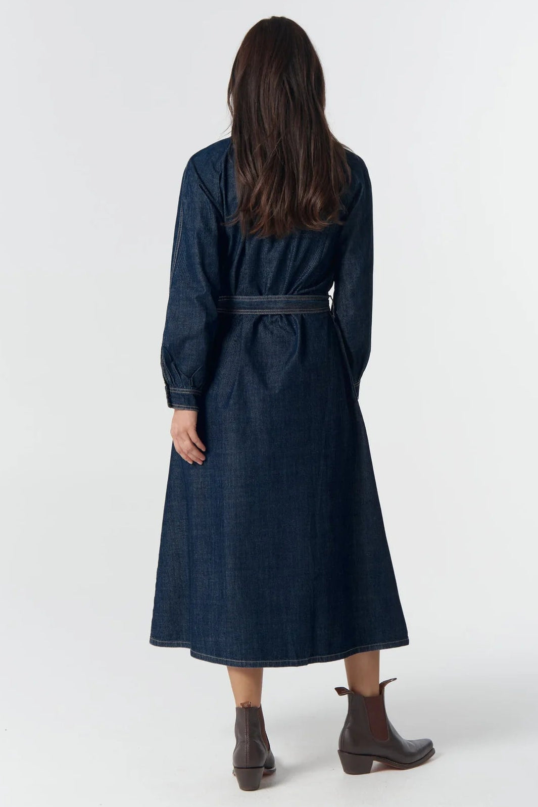 Woman wearing a long dark blue dress with a belt on a white background