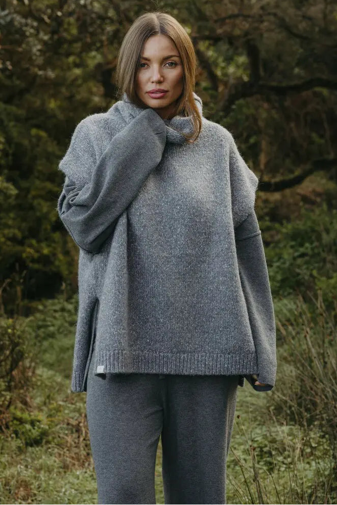 Woman wearing a gray sweater and pants standing in a natural setting