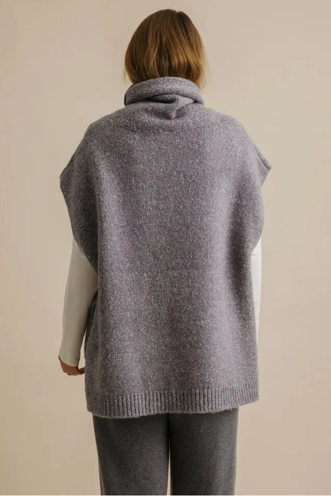 Person wearing a gray knitted vest on a beige background