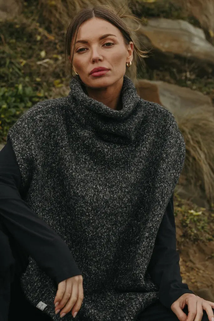Woman wearing a dark gray knitted vest outdoors with greenery in the background