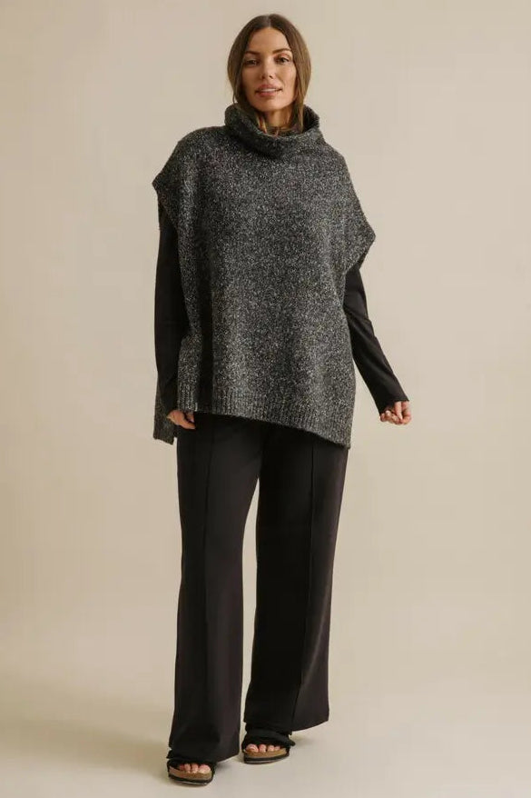 Woman wearing a dark gray poncho and black pants on a beige background