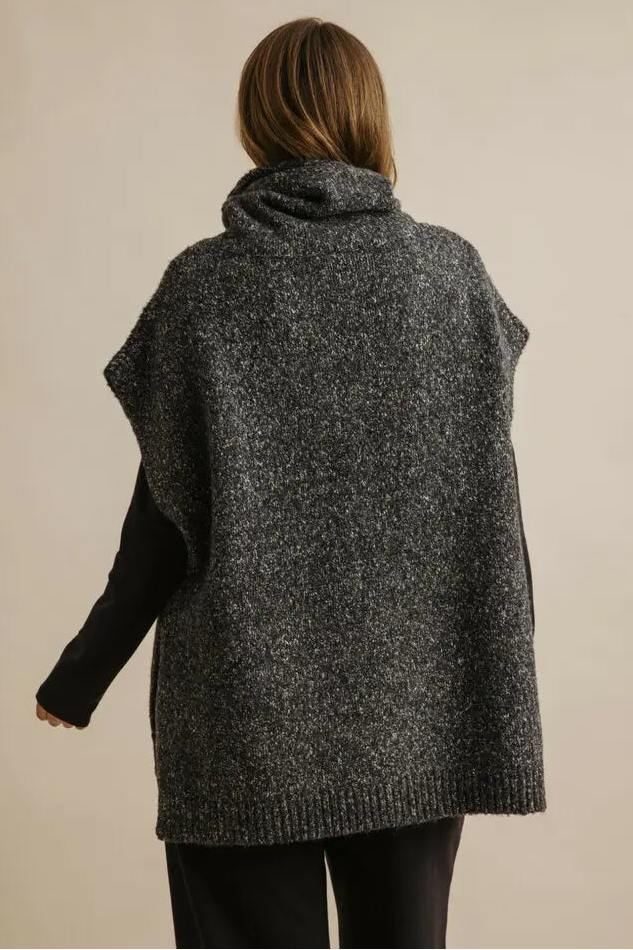 Person wearing a gray knitted vest on a beige background