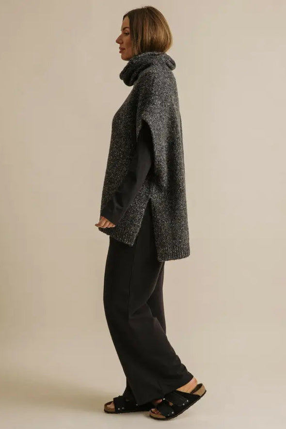 Person wearing a gray coat and black pants on a beige background