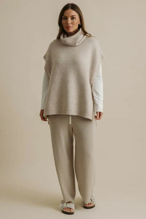 Woman wearing a light gray turtleneck sweater and pants on a beige background