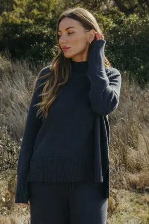 Woman in a navy outfit standing in a natural setting with trees and grass.