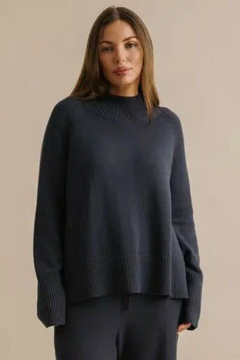 Woman wearing a dark blue sweater and pants on a beige background