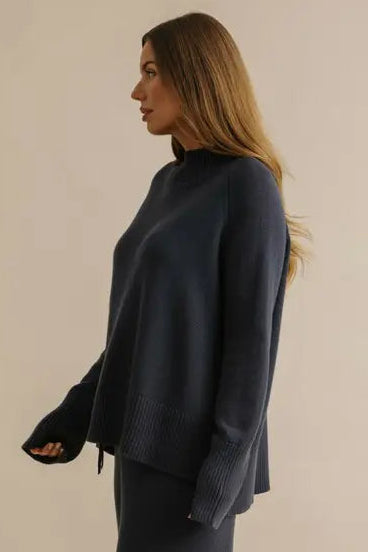 Woman wearing a dark blue outfit standing against a beige background