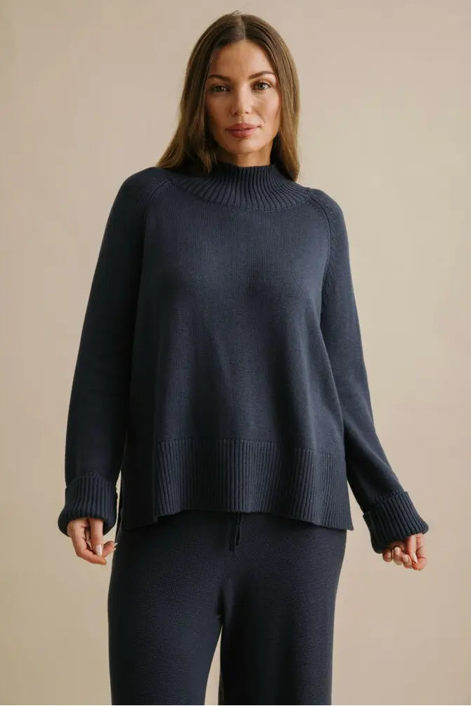 Woman wearing a navy sweater and pants against a beige background