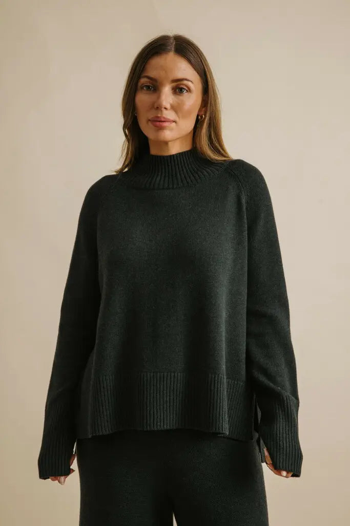 Woman wearing a dark green sweater against a beige background
