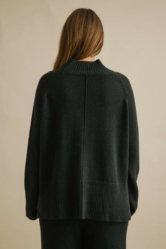Person wearing a dark green sweater against a beige background