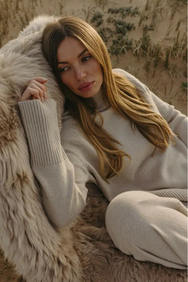 Woman in a beige sweater and pants sitting on a fur rug in a desert setting