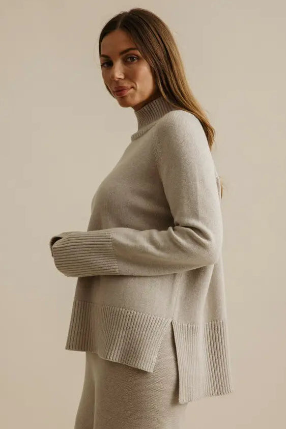 Woman wearing a beige sweater and skirt set against a plain background