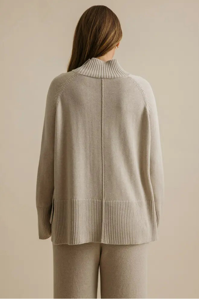 Person wearing a beige sweater and pants against a beige background