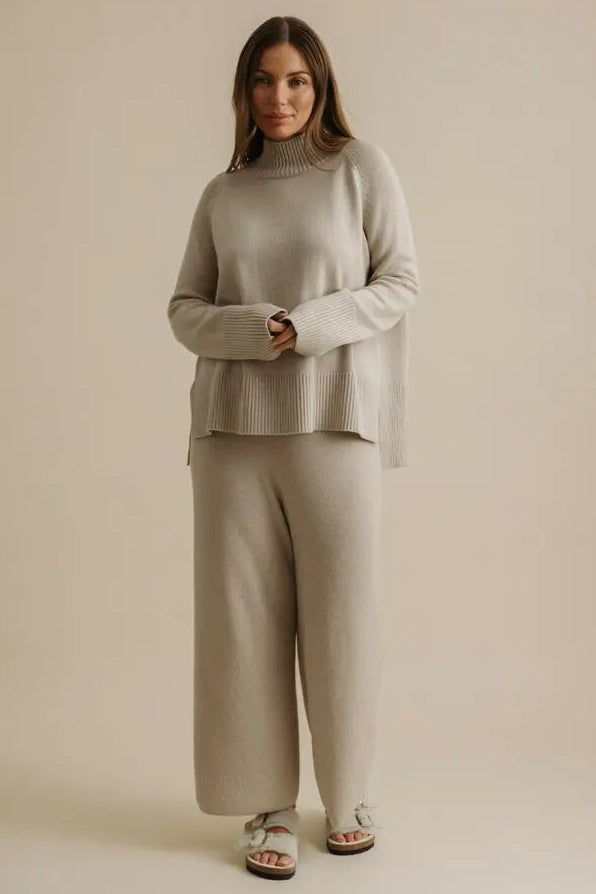 Woman wearing a beige sweater and pants set on a plain background