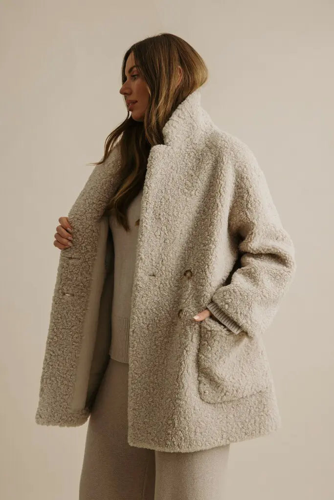 Woman wearing a beige teddy coat against a plain background
