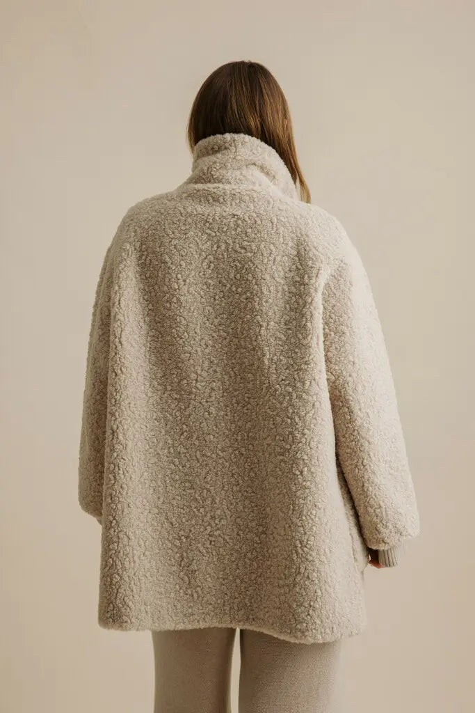 Person wearing a beige textured coat against a plain background