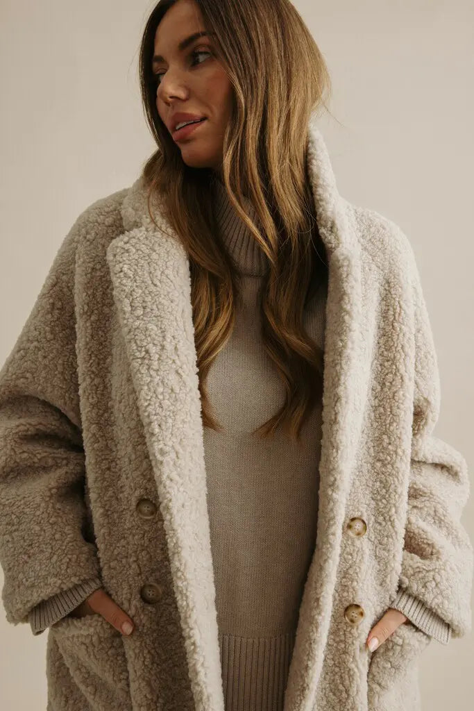 Woman wearing a beige sherpa-lined coat against a neutral background