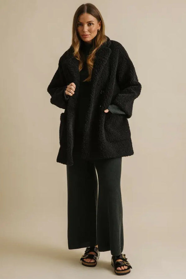 Woman wearing a black coat and pants on a beige background