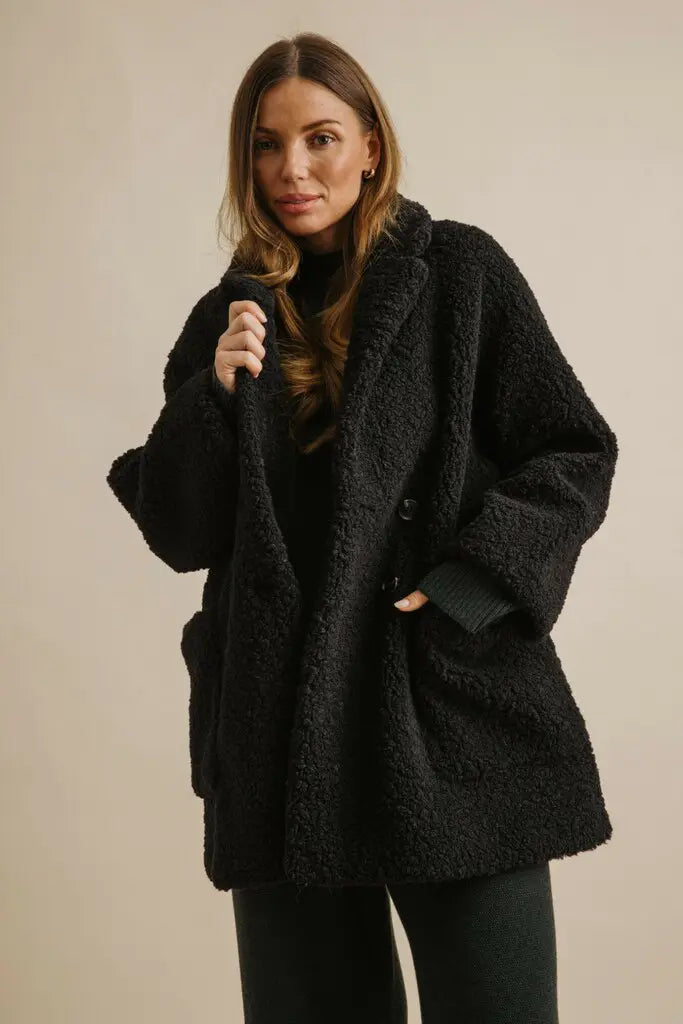 Woman wearing a black coat against a beige background