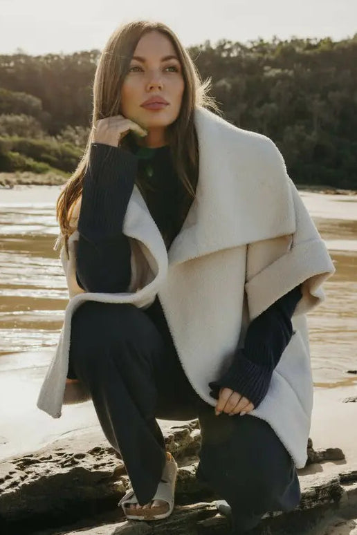 Woman in a white coat sitting on rocks by a body of water