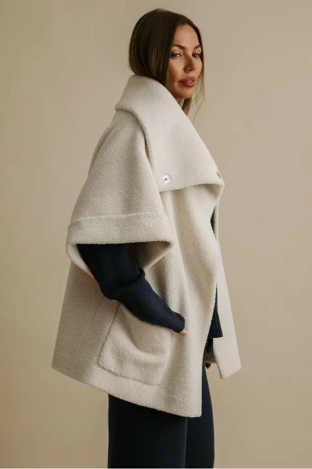 Woman wearing a beige cape against a beige background