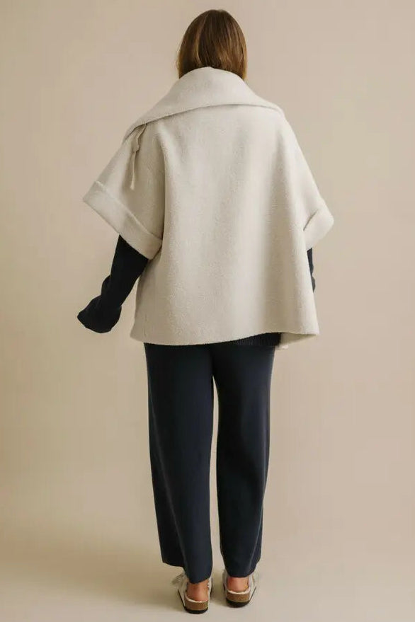 Person wearing a beige cape over dark clothing on a plain background