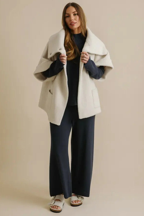 Woman wearing a white coat over a navy outfit on a beige background