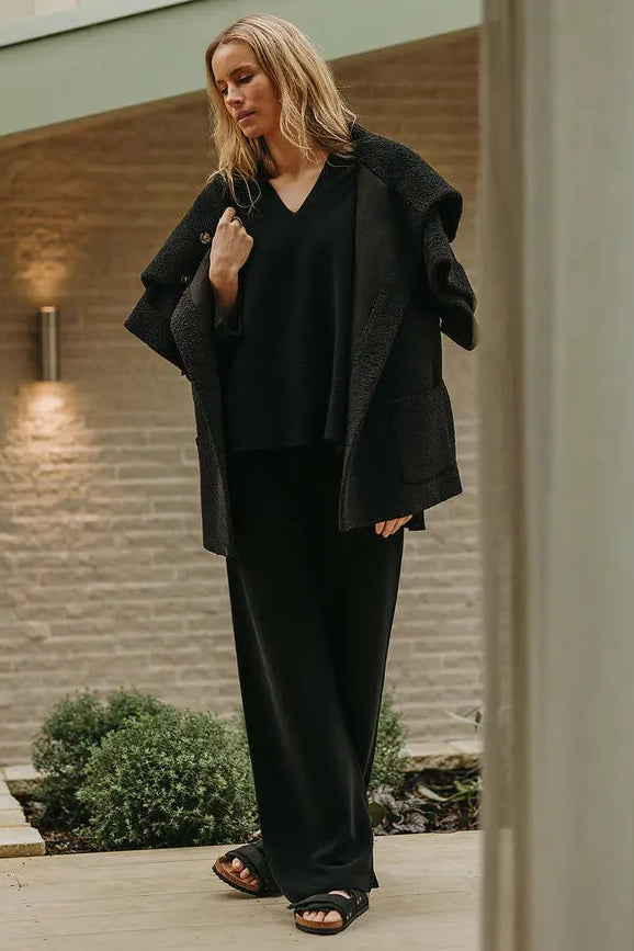Woman in black outfit standing on a wooden deck with a neutral background