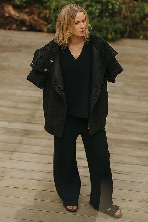 Person wearing a black outfit on a wooden deck with greenery in the background