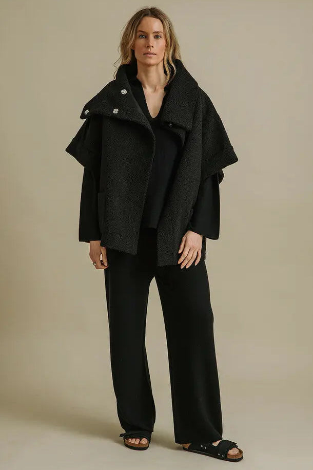 Woman wearing a black coat and pants against a beige background