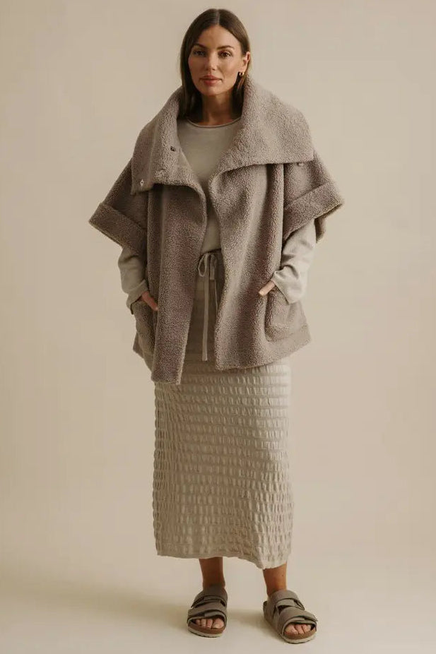 Woman wearing a long, textured coat over a dress on a beige background